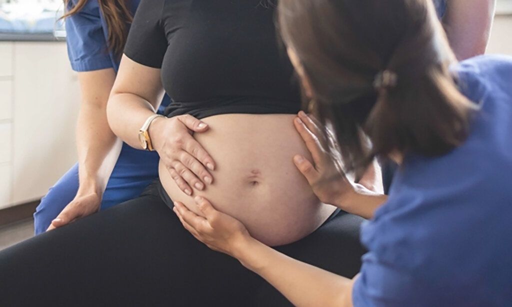 Hebamme tastet den Bauch einer schwangeren Frau ab