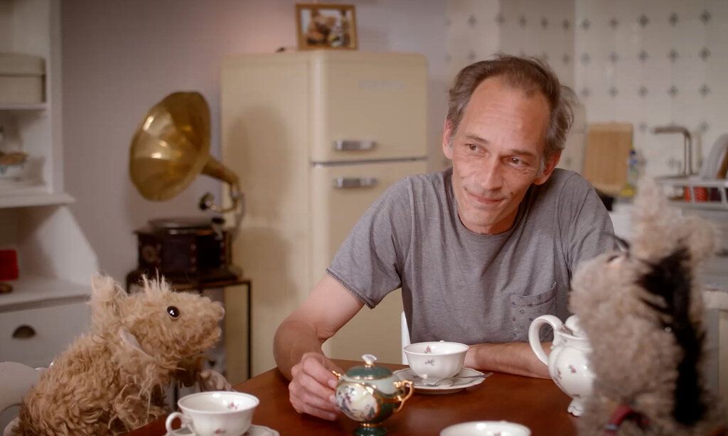 Mann sitzt mit Stofftieren am Kaffeetisch