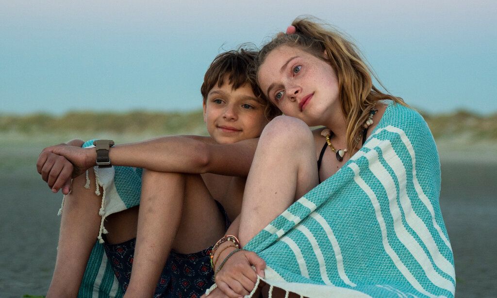 Ein Junge und ein Mädchen sitzen im Abendlicht am Strand, über den Schultern ein Handtuch