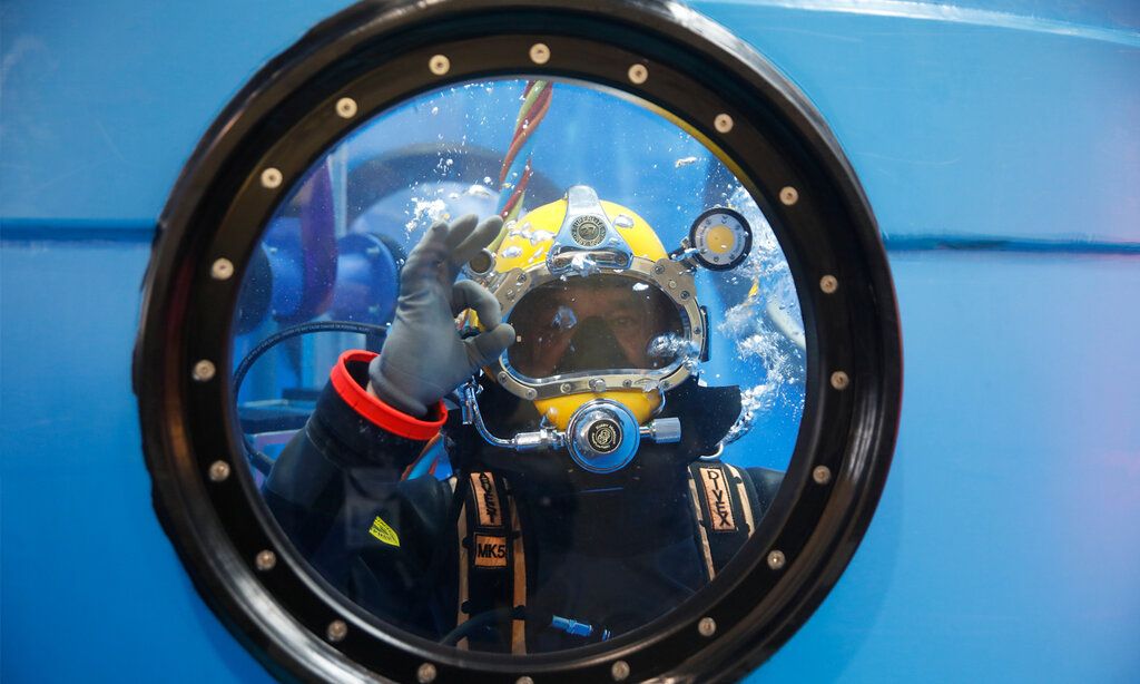 durch ein Bullauge sieht man einen Taucher, der ein Handzeichen gibt, dass alles perfekt ist