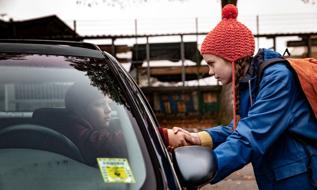 ein Mädchen steht an einem Auto, in dem ein Junge sitzt, beide geben sich die Hand