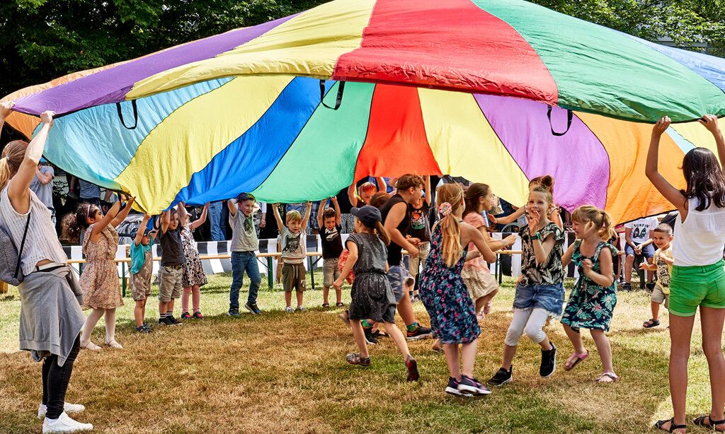 Kinder spielen auf einer Wiese und schwingen einen großen runden Stoff