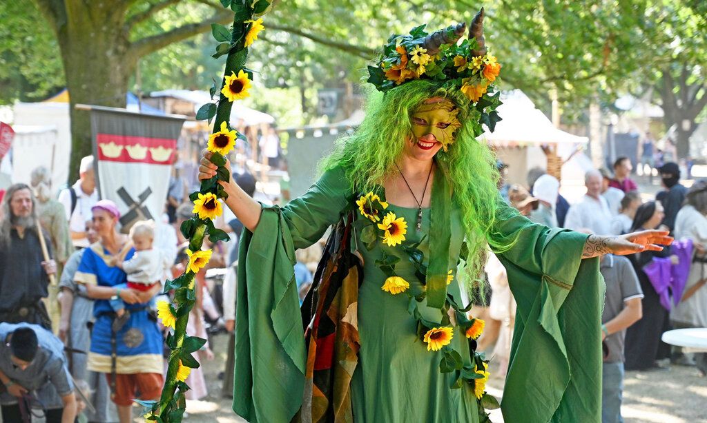 Eine Frau ist als Fee oder Waldgeist verkleidet, im Hintergrund Mittelaltermarkt mit Besucher:innen
