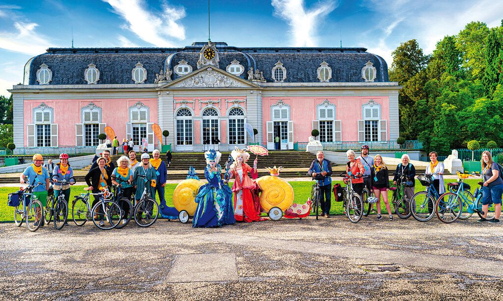 Fahrradfahrer und Frauen in barocken Kostümen vor Schloss Benrath