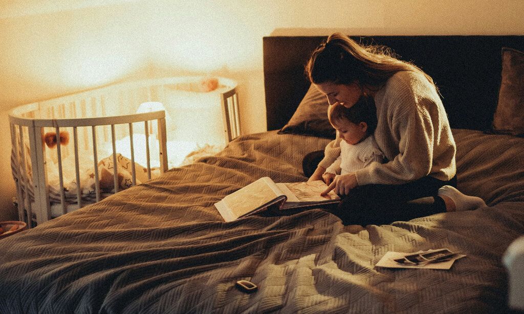 Mutter sitzt mit Baby auf dem Bett und guckt sich ein Buch an