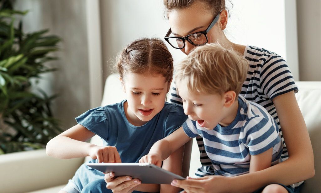 junge Mutter mit kleinem Sohn und Tochter, die auf dem Sofa sitzen und auf das Tablet schauen