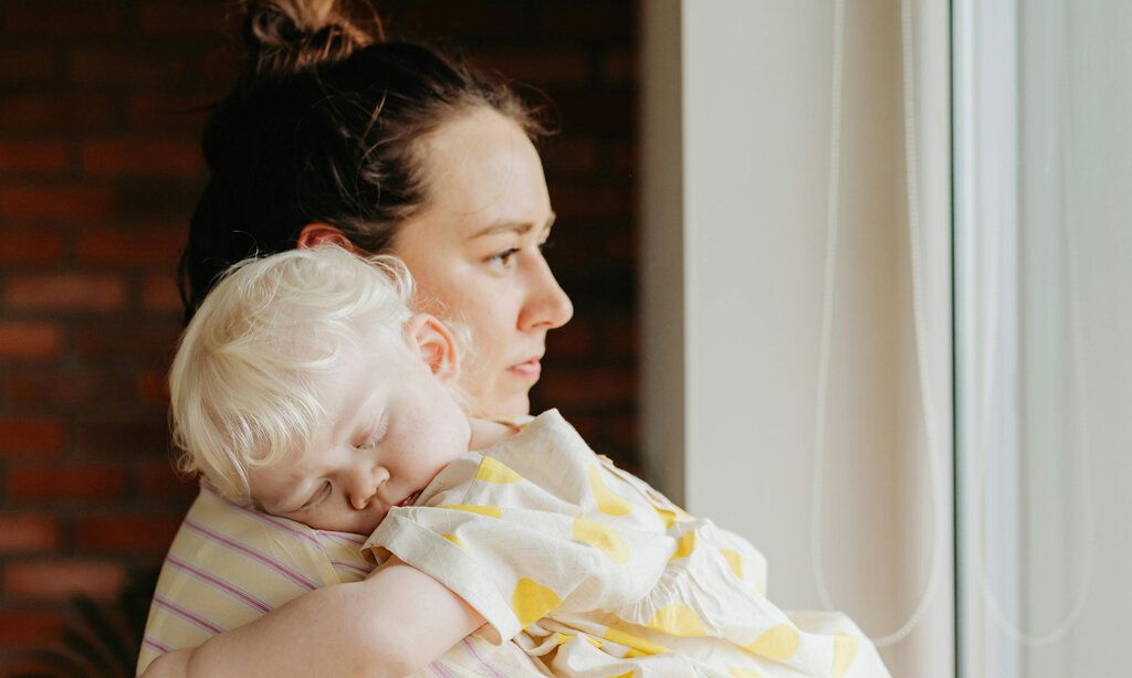 Mutter guckt nachdenklich und hat ein Baby auf dem Arm