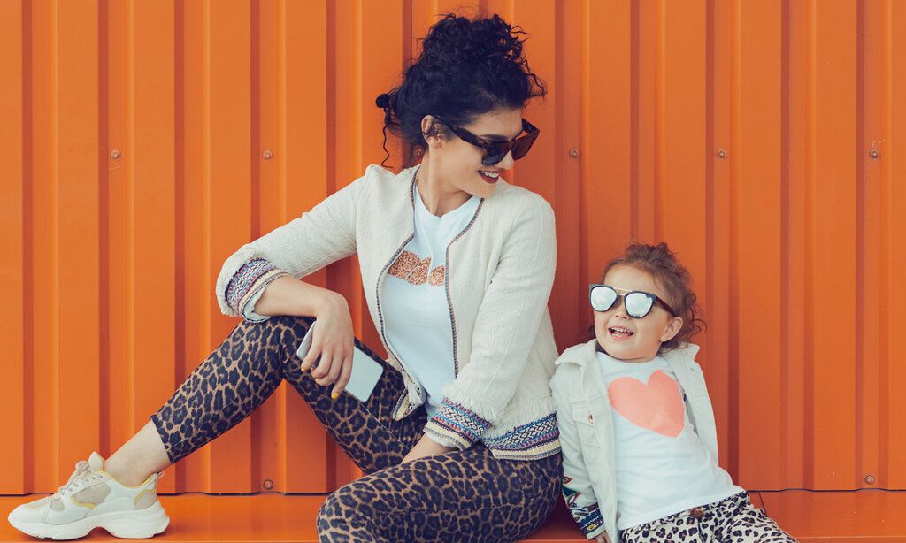 Mutter und Tochter vor oranger Blechwand, beide tragen Hosen mit Leoprint und Sonnenbrille
