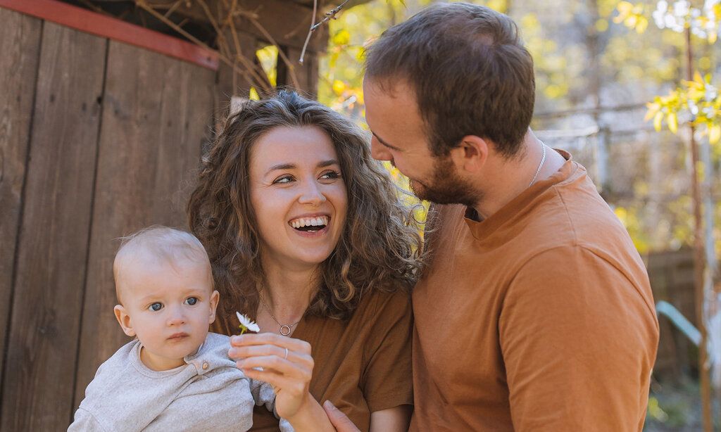 junges Elterpaar mit Baby vor Holzhütte im Frühling