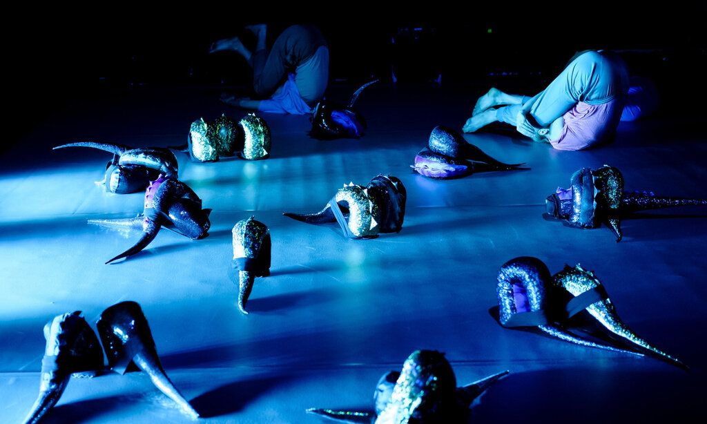 My tail and I Tanzperformance, blaue Beleuchtung, zwei Kinder liegen mit den beinem über dem Kopf auf der Bühne, glitzernde Dino-Schwänze liegen herum