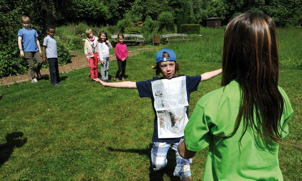 Ein Junge läuft über eine Wiese zu einer Frau, andere Kinder gucken zu
