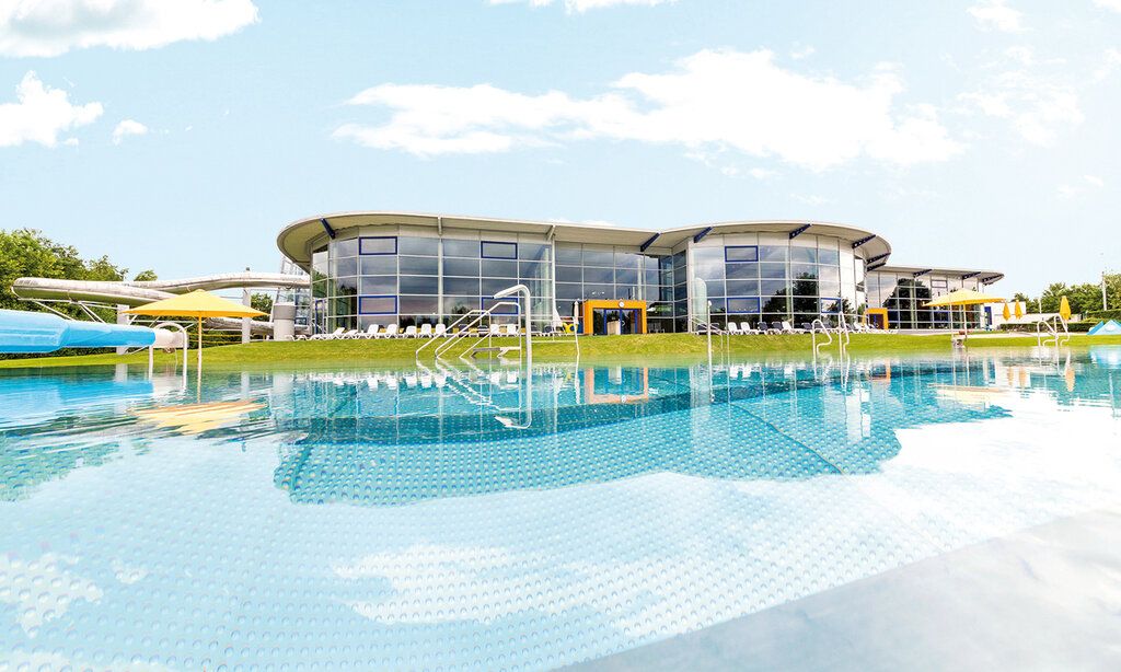 Der Außenbereich des Neanderbads mit Blick über das Außenbecken auf das Genbäude des Hallenbades im Sommer