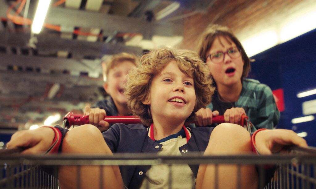 Ein Junge sitzt in einem Einkaufswagen und wird von zwei anderen Kindern geschoben