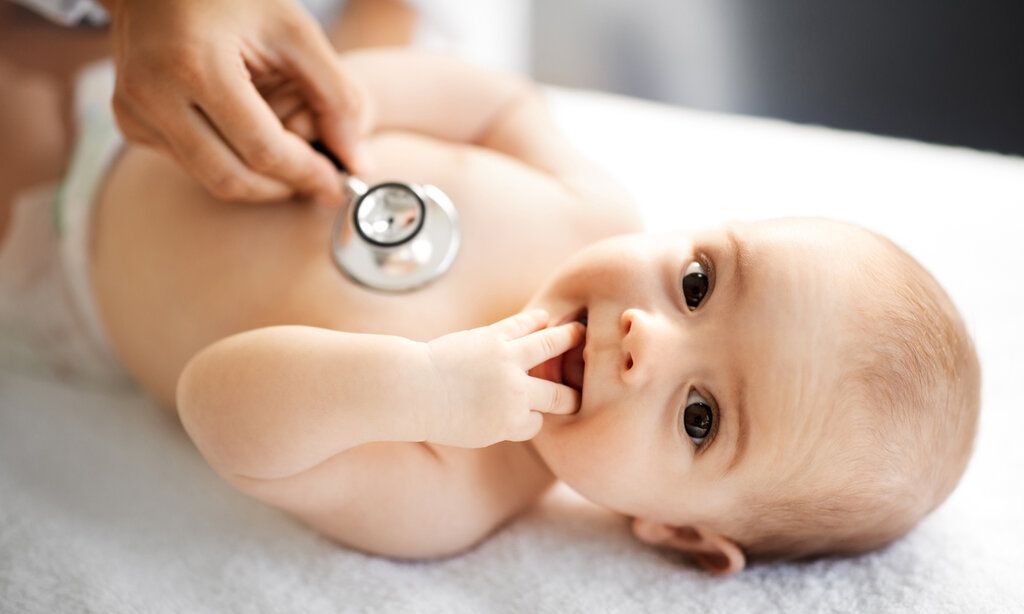 Ein Baby liegt auf dem Rücken und wird mit einem Stethoskop abgehört