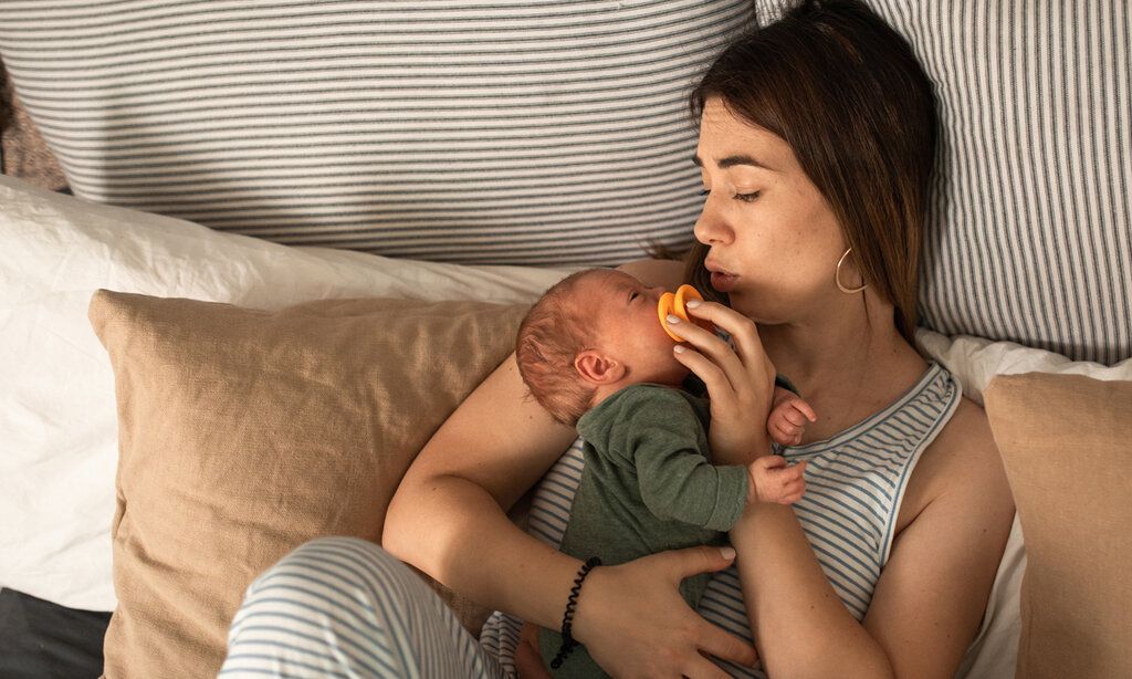 Eine Frau sitzt im Bett mit vielen Kissen und hält ihr neugeborenes Baby im Arm