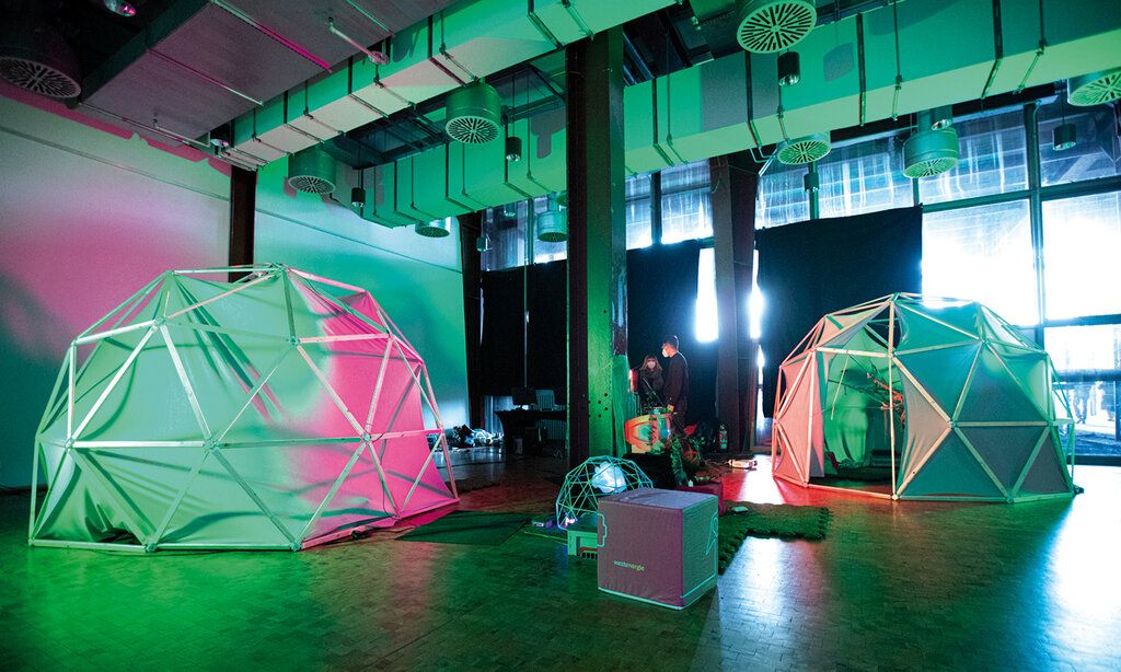 Halle in der zeltartige Objekte und zwei Menschen stehen, Beleuchtung grün/pink