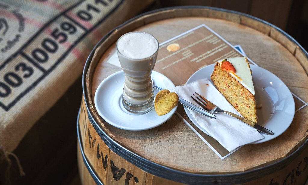 Ein Glas Milchkaffee und ein Rüblikuchen auf einem alten Fass