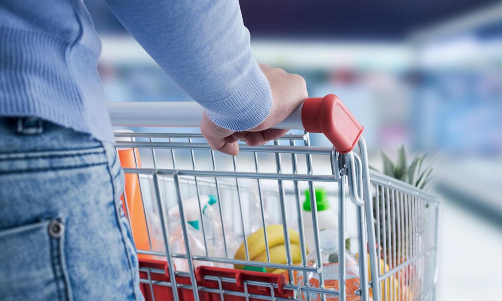 Detailansicht von einer Frau, die einen Einkaufswagen schiebt, im Hintergrund ein Supermarkt unscharf