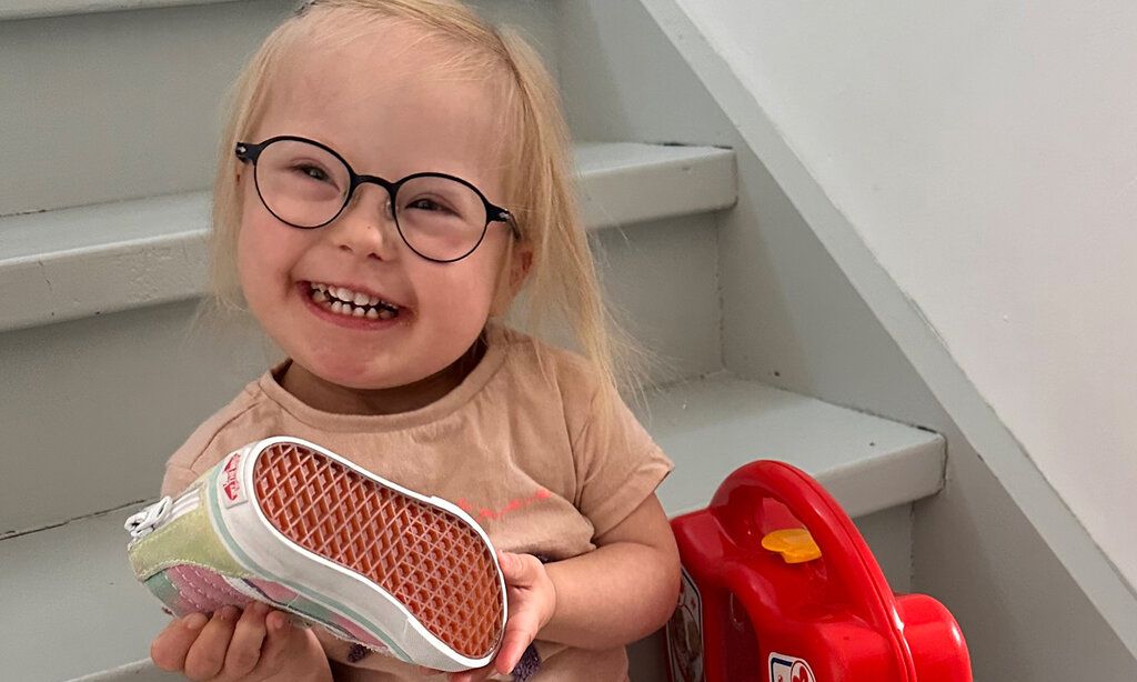 kleines Mädchen mit Down-Syndrom sitzt auf einer Treppe und hält einen Turnschuh in der Hand
