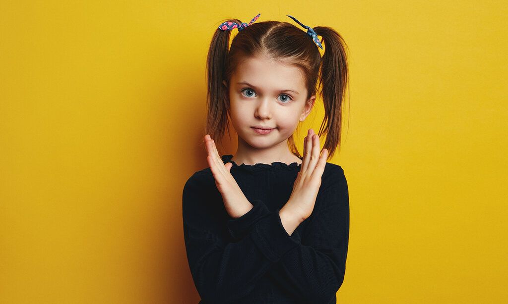 Mädchen mit Zöpfen, Handbewegung: Hände über kreuz, Hintergrund gelb
