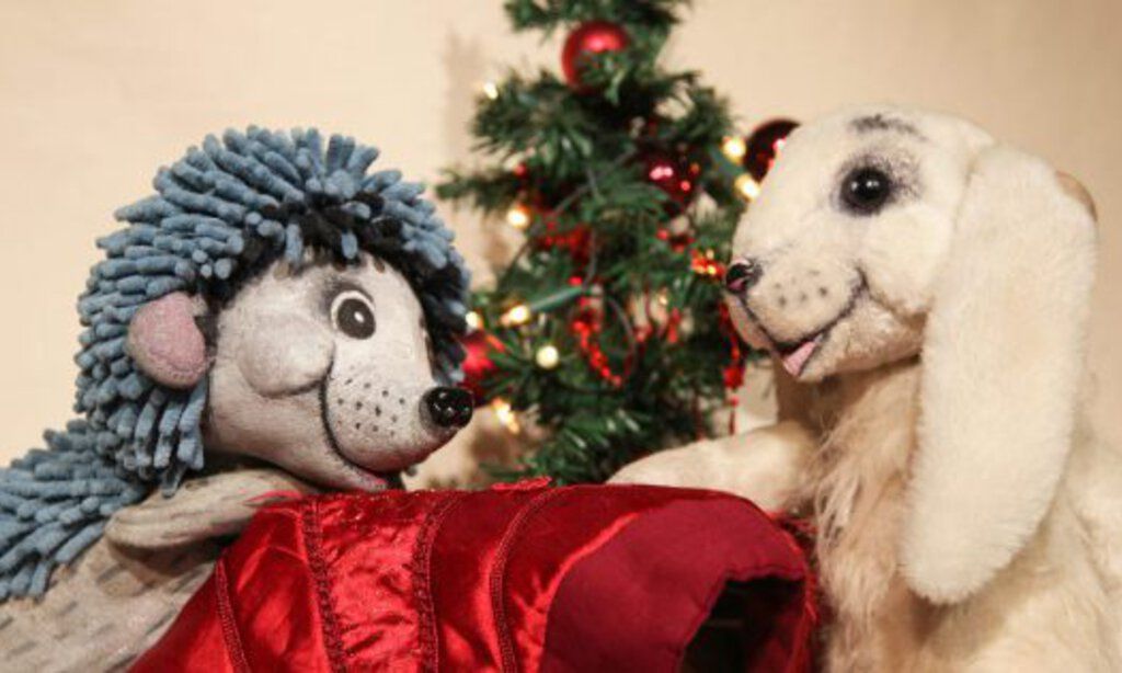 Szenenbild mit Hasen- und Igelpuppe vor einem Weihnachtsbaum aus „Mein Weihnachtsgeschenk für dich“ des August Theaters Dresden.