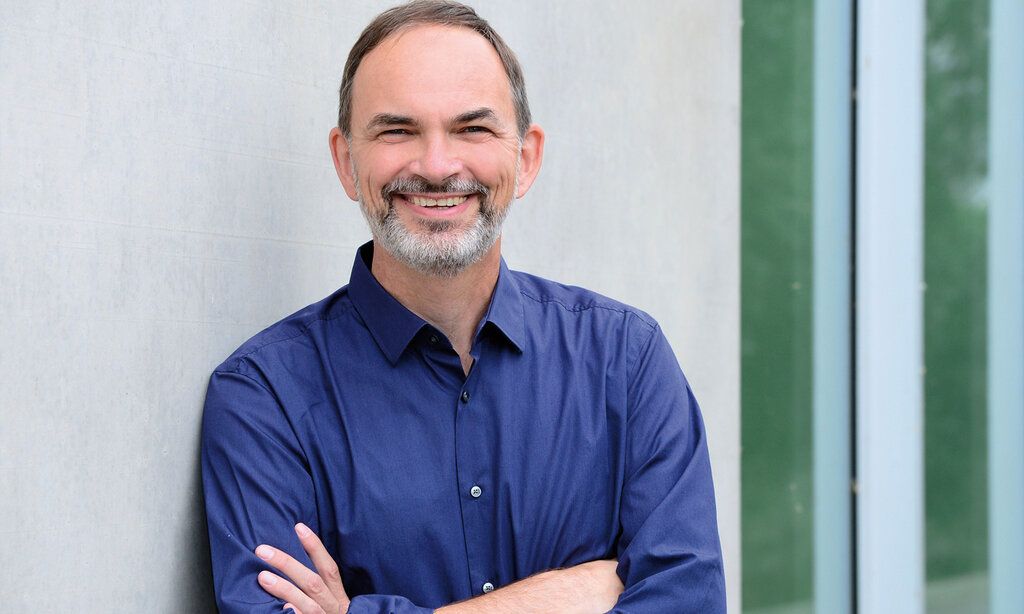 Prof. Dr. Ulrich Reinhardt steht mit verschränkten Armen vor grauer Mauer
