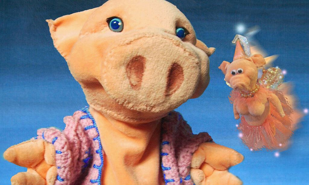 großes Plüschschwein mit rosa Häkelweste im Vordergrund, daneben fliegt eine kleine Schweine-Fee, der Hintergrund ist blau