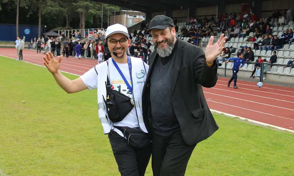 Rabbi Malinsky und Veranstaltungsleiter Redouan Aoulad Ali stehen Arm in Arm, im Hintergrund ein Sportplatz mit einer Tribüne mit Publikum