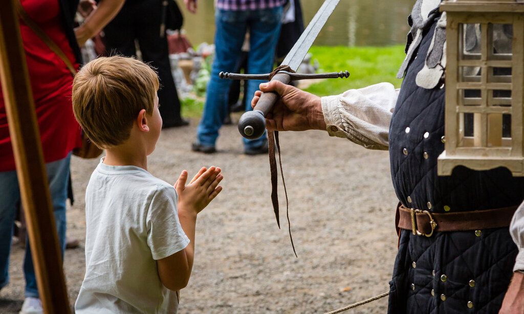 ein kleiner Junge steht bei einem Ritter, der ihm ein Schwert reicht