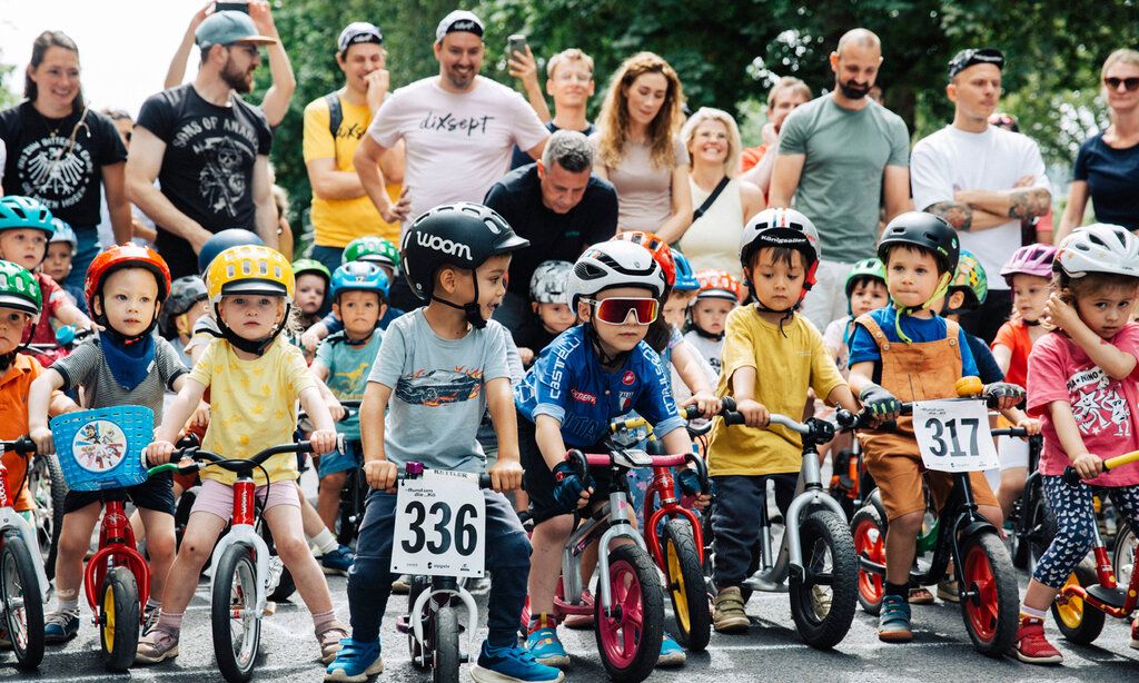 eine Gruppe von Kleinkindern steht mit Laufrädern am Start für ein Laufrad-Rennen, im Hintergrund die Eltern