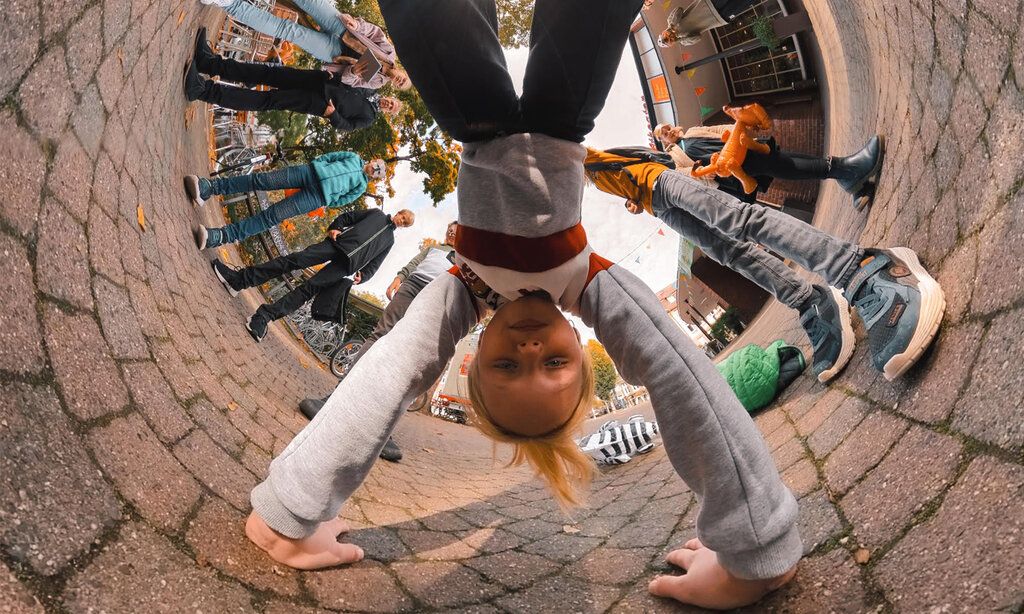 Mädchen macht Handstand auf dem Schulhof, mit 360°-Kamera fotografiert und daher rund gebogen