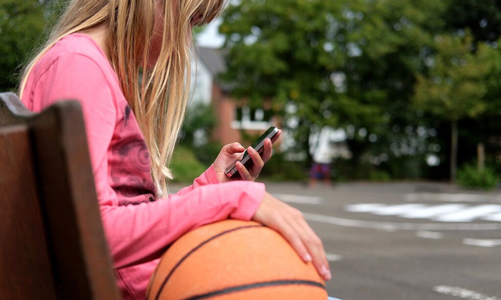 Junges Mädchen sitzt auf einer Bank und nutzt Smartphone