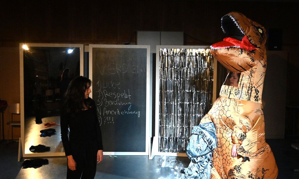 Zwei Frauen auf einer Bühne, ein davon trägt ein Dinosaurier-Kostüm
