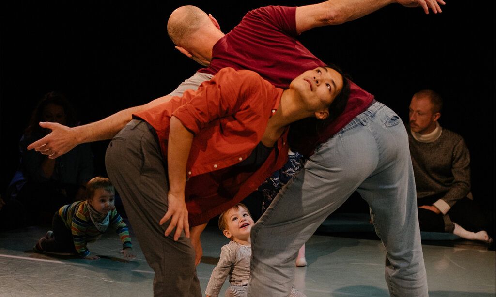eine Tänzerin und ein Tänzer tanzen miteinander und ein Kleinkind sitzt lachend auf der Bühne