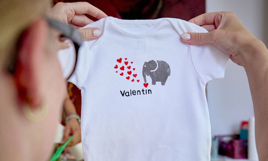 Frau hält selbstgestalteten Babybody in den Händen, auf dem Body ist ein Elefant mit roten Herzchen abgebildet und Schrift: Valentin