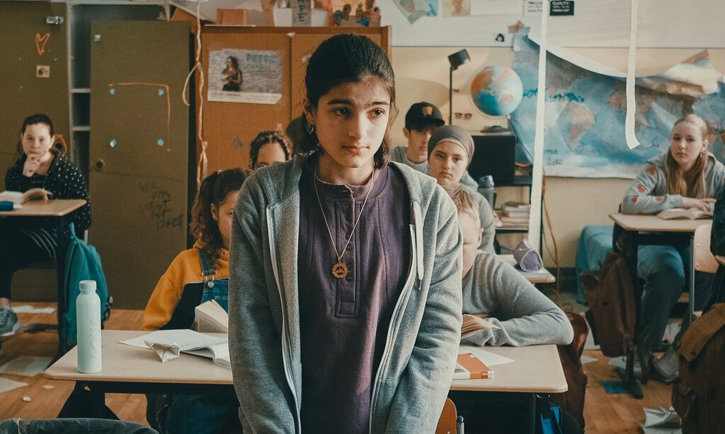 ein Mädchen steht in einer Schulklasse und guckt traurig