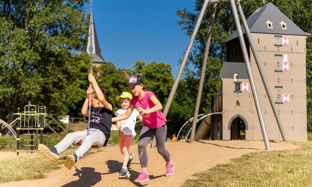 Drei Kinder spielen auf einem Spielplatz mit Seilbahn im Landschaftspark in Monheim am Rhein
