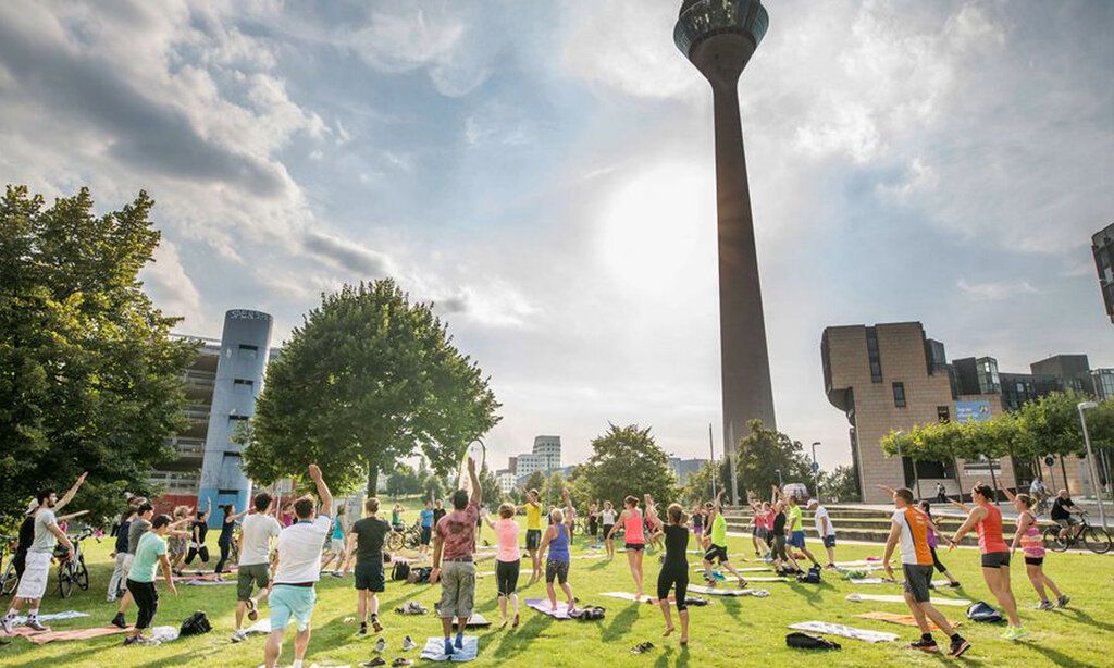 Sport im Park-Kurs mit Teilnehmenden, die auf der Wiese vor dem Rheinturm turnen