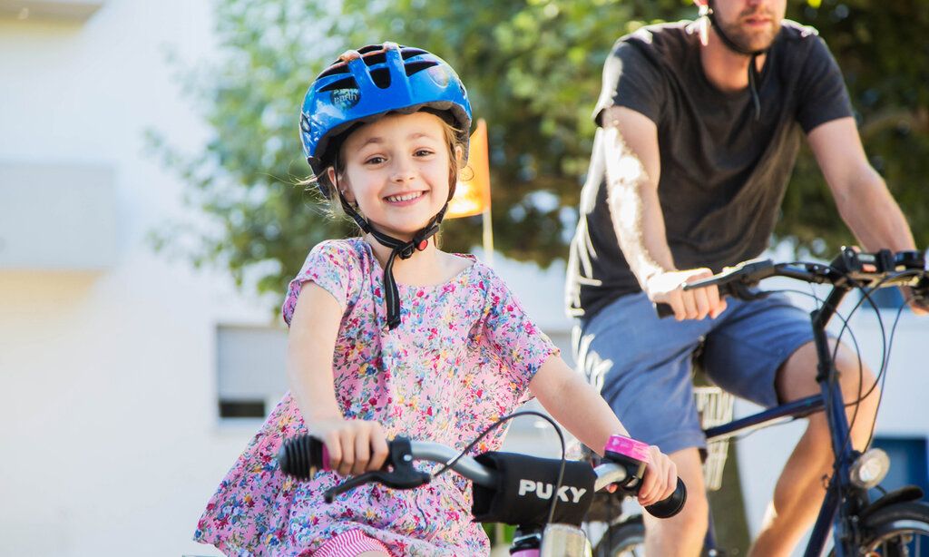 Mädchen mit Helm fährt Fahrrad, im Hintergrund ein Mann auf einem Fahrrad