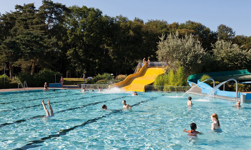 Freibad mit gelber Wasserrutsche, im Hintergund Bäume