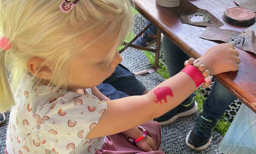Kleines Mädchen mit einem roten Mammut-Tattoo auf dem Arm