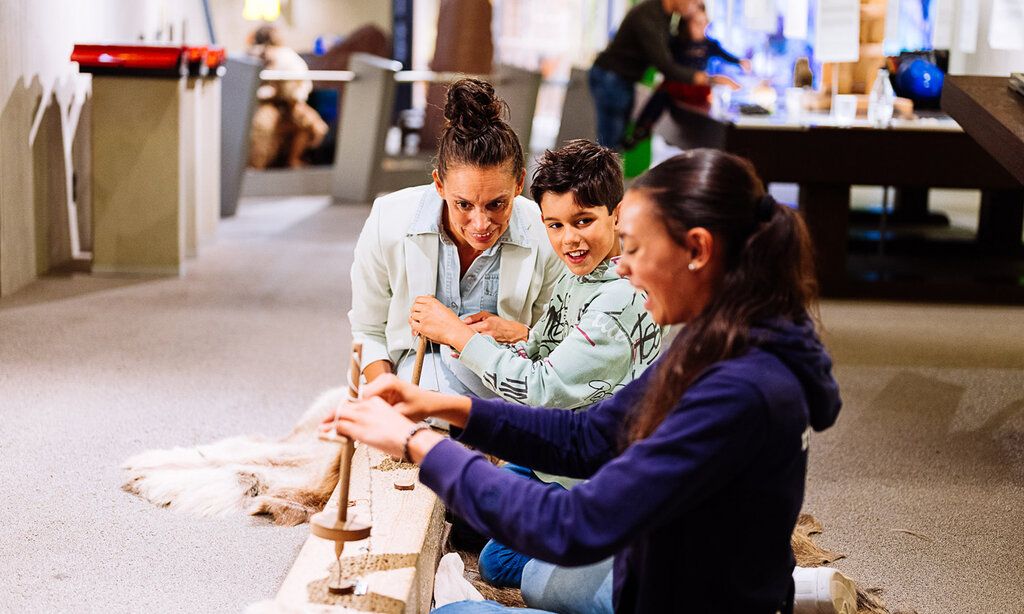 Zwei Kinder und ihre Mutter werkeln in der Steinzeitwerkstatt im Neanderthal Museum