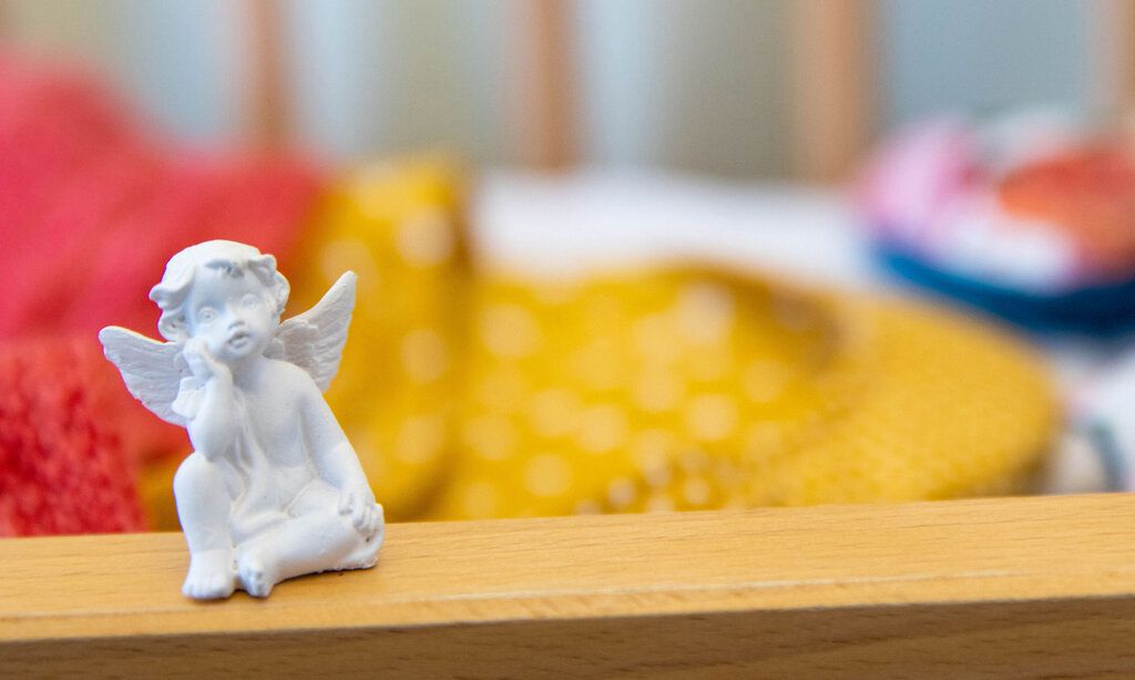 Eine kleine Engelsfigur, im Hintergrund ein leeres Babybett