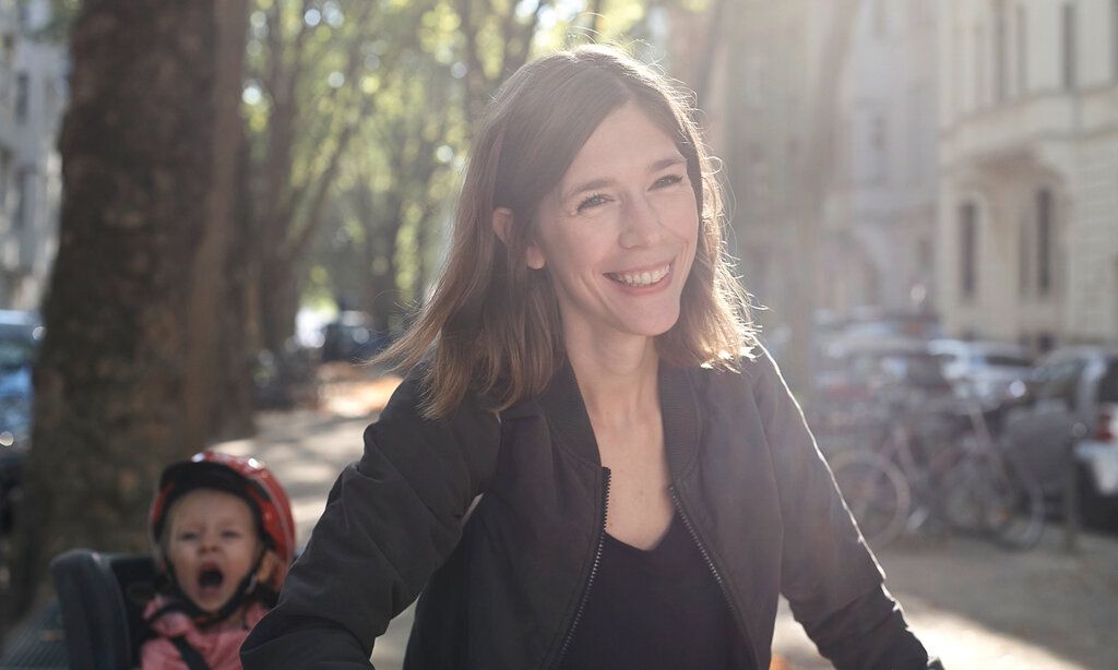 Junge Frau auf einer sommerlichen Straße, Kind im Fahrradkindersitz hinter ihr