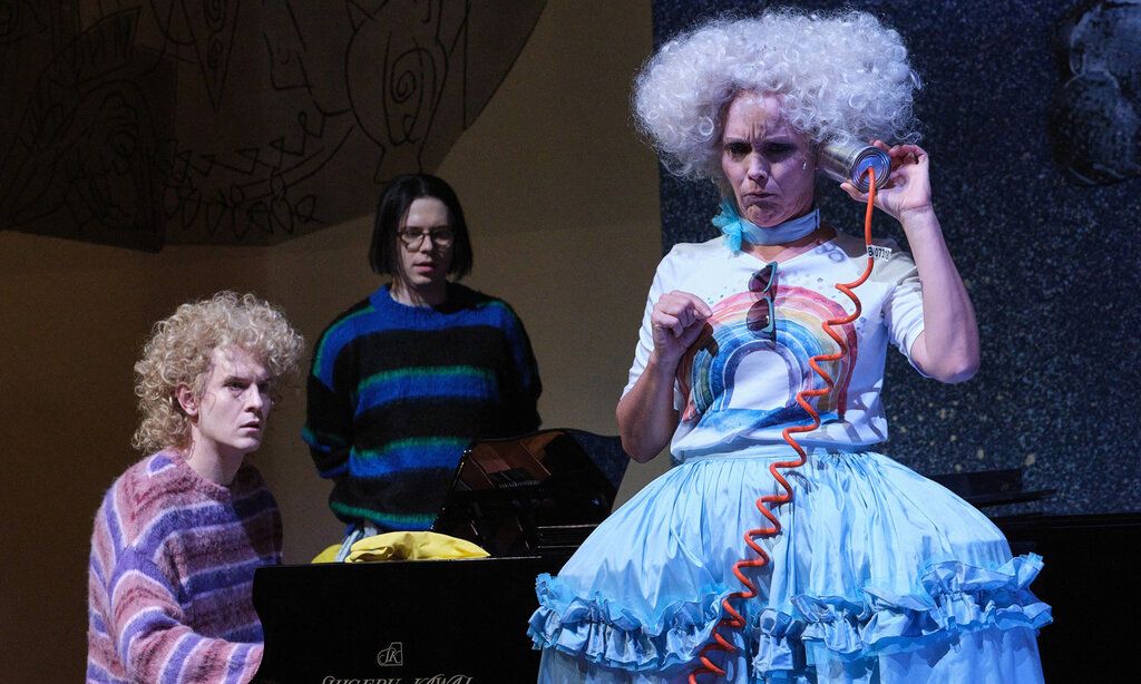 Szene aus der Oper Holle!, Frau Holle telefoniert mit einer Blechdose, zwei Personen gucken zu