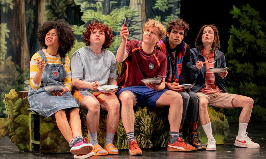 Fünf Jugendliche sitzen auf einer Theaterbühne vor einer Waldkulisse