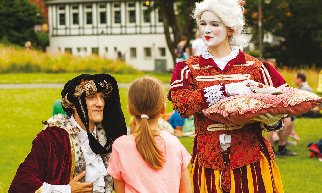 zwei märchenhaft verkleidete Schauspieler stehen mit einem Kind in einem Park