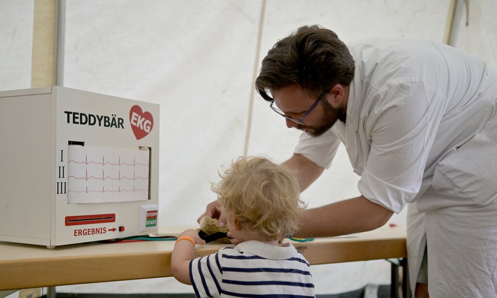 Arzt untersucht einen Teddybären, kleines Kind schaut zu