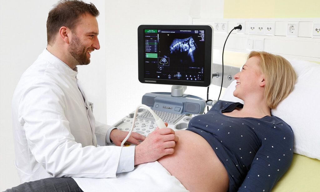Ein Arzt macht eine Ultraschalluntersuchung bei einer Schwangeren, beide lächeln