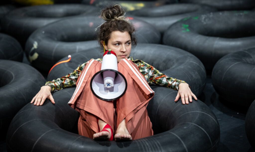 Frau sitzt mit einem Megaphone in einem schwarzen Reifen, um sie herum weitere schwarze Reifen